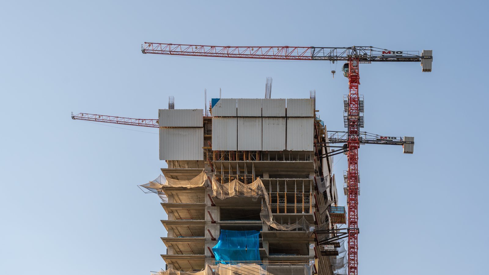Topo de um edifício residencial em estrutura de concreto, com duas gruas, contra o céu azul